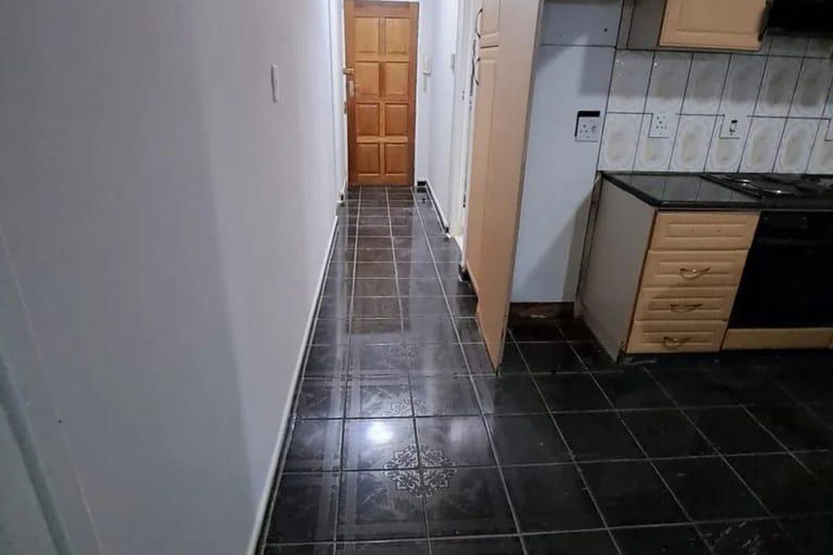 A functional kitchen area featuring dark tiled flooring, built-in wooden cabinetry, and integrated appliances, leading into a hallway with a wooden door.