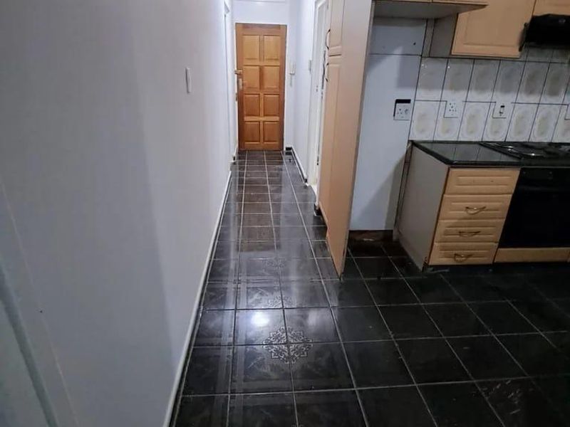 A functional kitchen area featuring dark tiled flooring, built-in wooden cabinetry, and integrated appliances, leading into a hallway with a wooden door.
