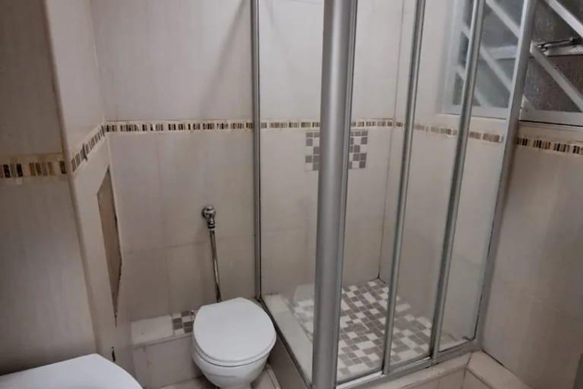 A compact bathroom featuring a shower enclosure, toilet, and pedestal basin with tiled finishes, requiring minor repairs to wall tiling.