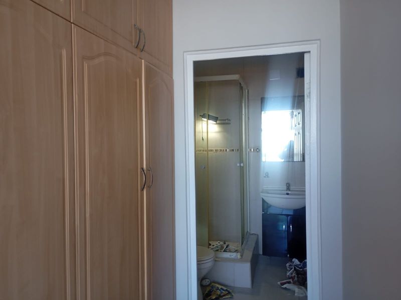 Bedroom featuring built-in cupboards and an adjoining en-suite bathroom with a shower and vanity basin.