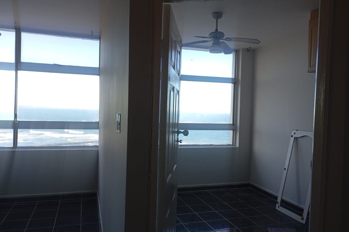 An empty bedroom featuring tiled flooring, a ceiling fan, and large windows offering expansive ocean views.