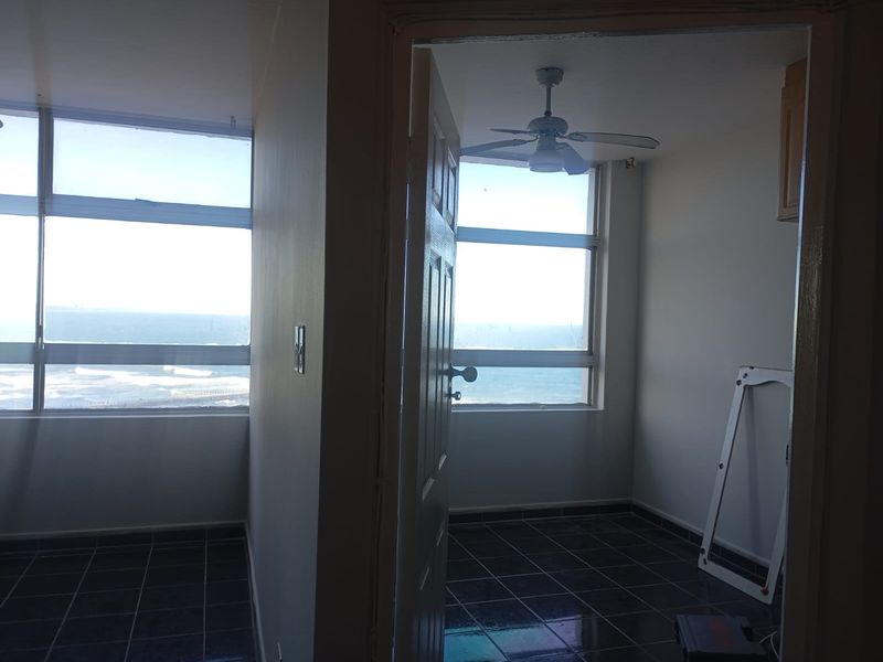 An empty bedroom featuring tiled flooring, a ceiling fan, and large windows offering expansive ocean views.