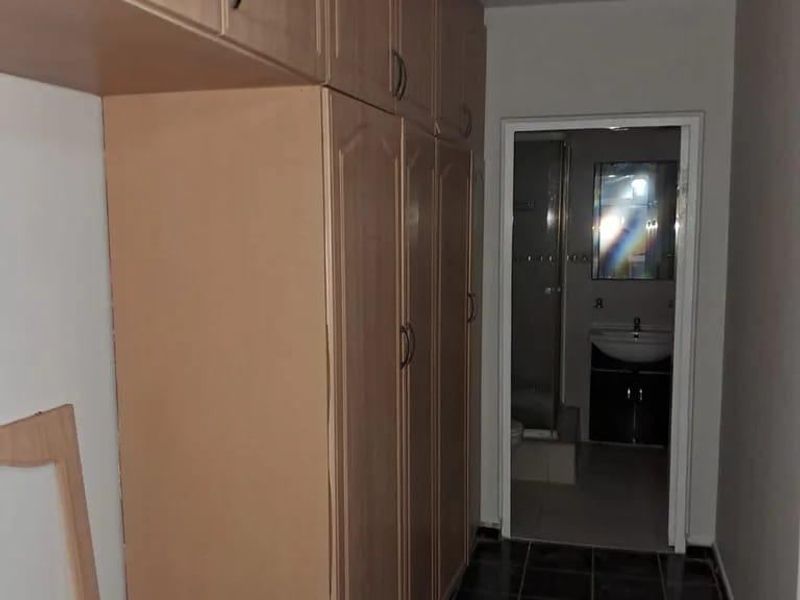 A hallway featuring built-in wooden cabinetry and dark tiled flooring, leading into a bathroom area.