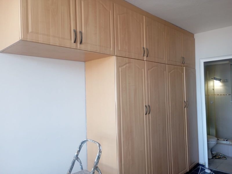 A bedroom featuring extensive light wood-finish built-in cupboards and overhead storage units, providing ample integrated storage space.