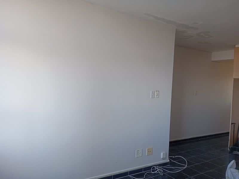 An empty open-plan living area featuring dark tiled flooring and visible ceiling water damage, offering a blank canvas for renovation.