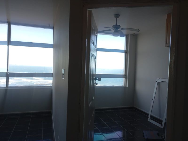 An empty bedroom featuring tiled flooring, a ceiling fan, and large windows offering expansive ocean views.