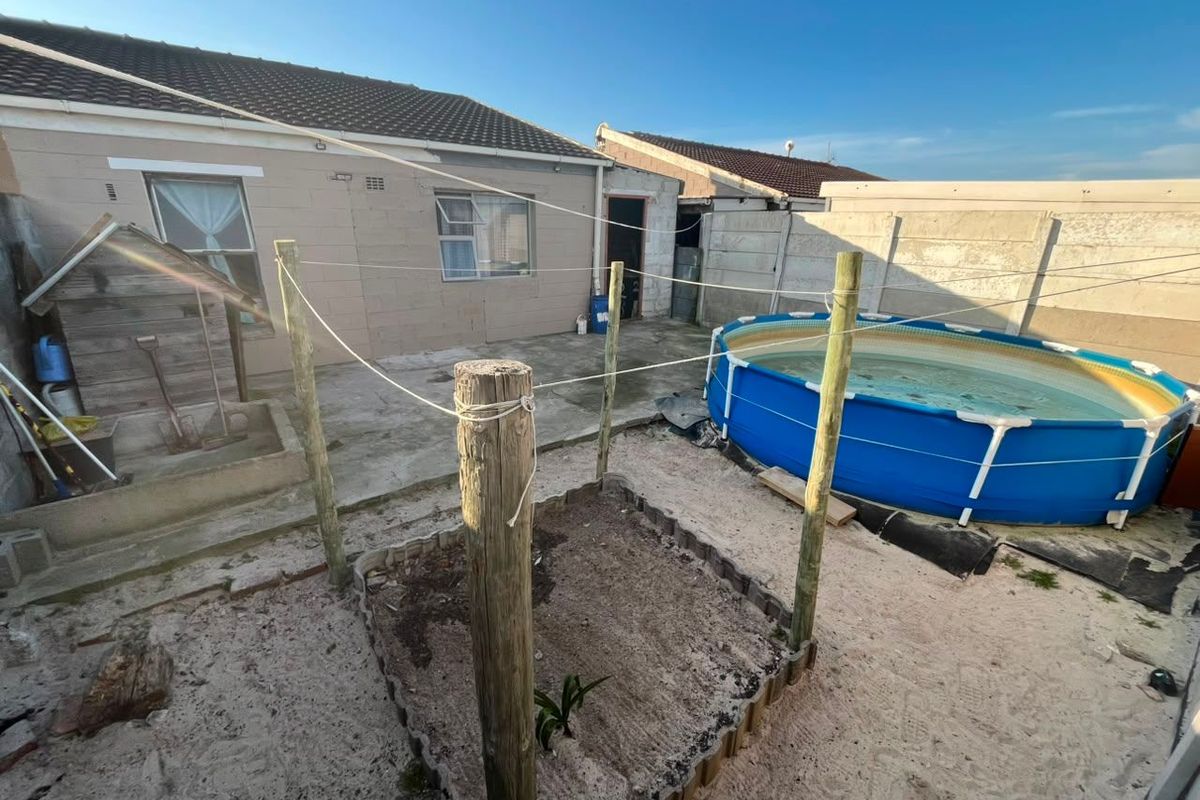 Rear exterior area featuring a concrete block house, precast boundary walls, and a sandy yard space with clothesline infrastructure.