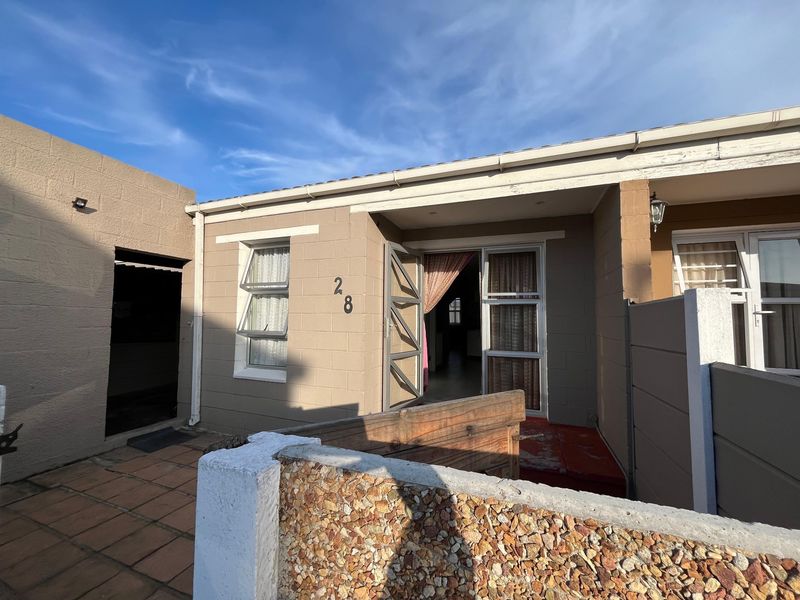 Front entrance view of a residential property featuring concrete block construction, tiled patio area, and aluminium window and door frames.