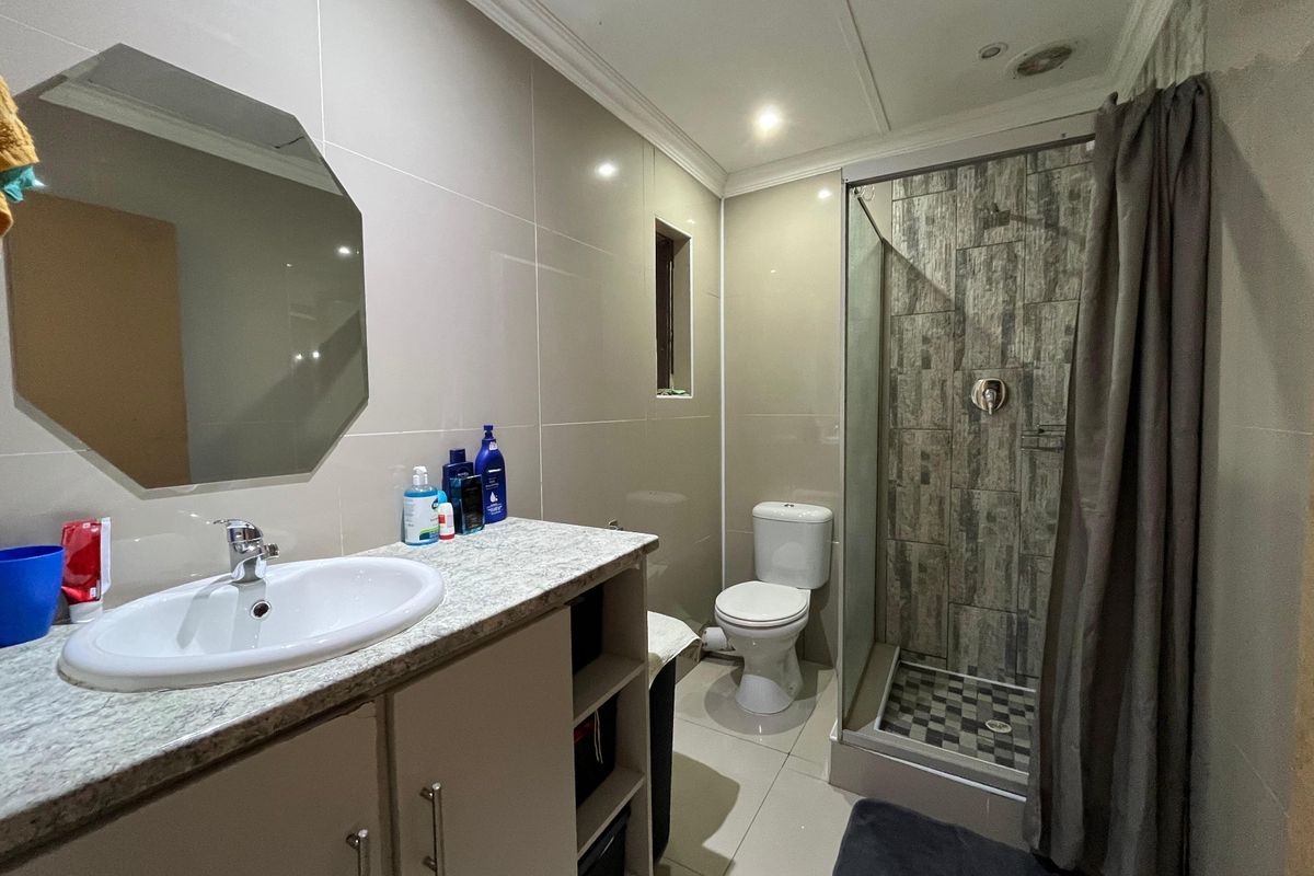 A functional bathroom featuring a vanity with basin, a toilet, and a shower enclosure with tiled finishes and modern lighting.