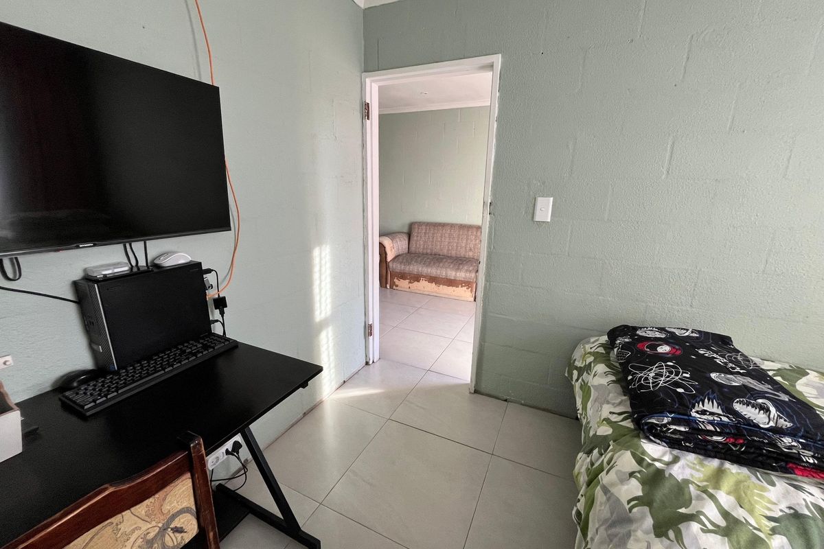 A bedroom featuring tiled flooring and painted block walls, with an adjoining room visible through the doorway.