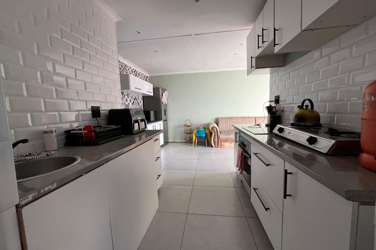 A galley-style kitchen featuring white cabinetry, subway tile backsplash, stone countertops, and a gas hob, leading into an open-plan living area.