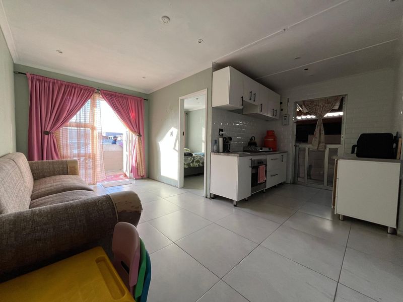 Open-plan living area featuring tiled floors, a compact kitchen with built-in cabinetry, and direct access to an outdoor patio area.