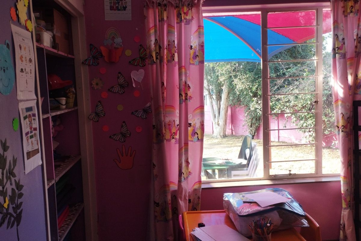 A bedroom featuring built-in shelving and a window with security bars, overlooking a garden area.