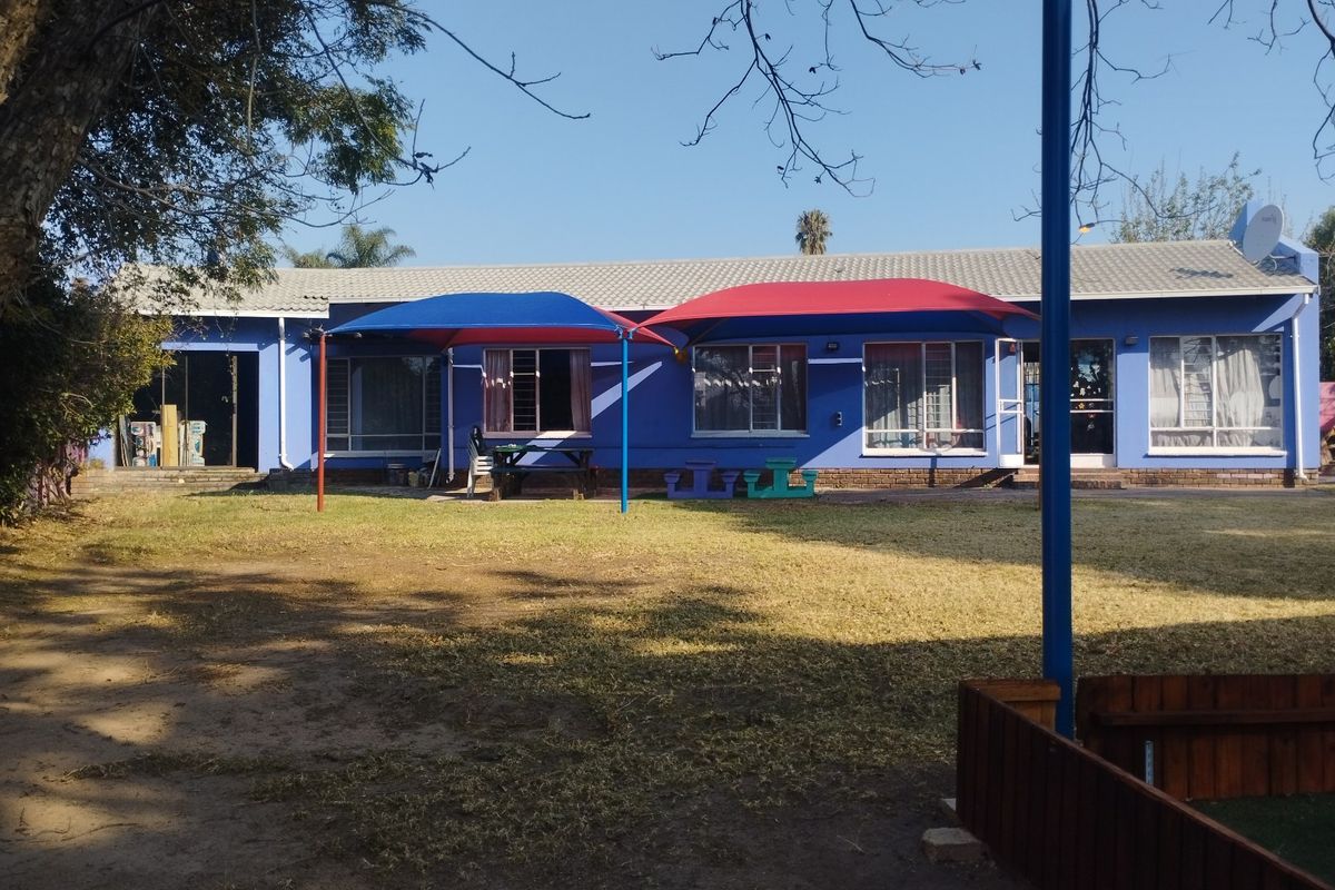 Rear view of a commercial property featuring a large lawn area, shade sails, and a tiled roof structure.