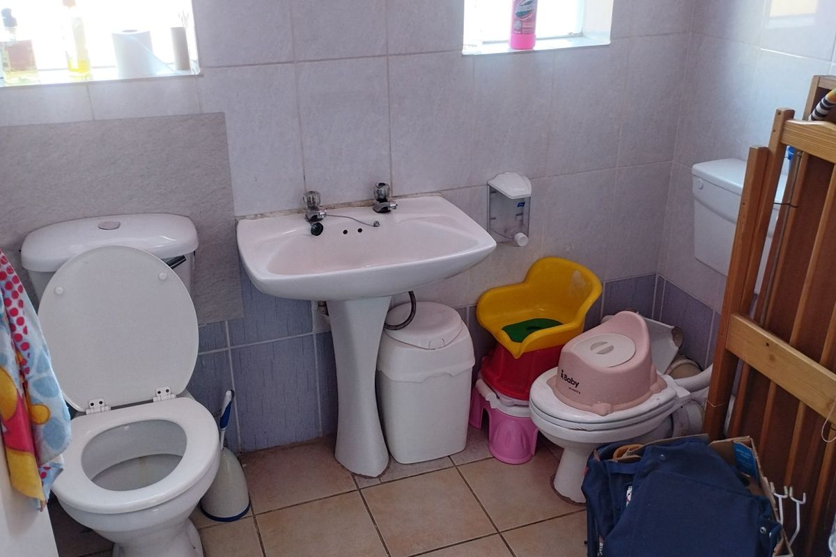 A functional bathroom featuring a pedestal washbasin, toilet, and tiled finishes. The space requires maintenance and updating to improve its overall condition.