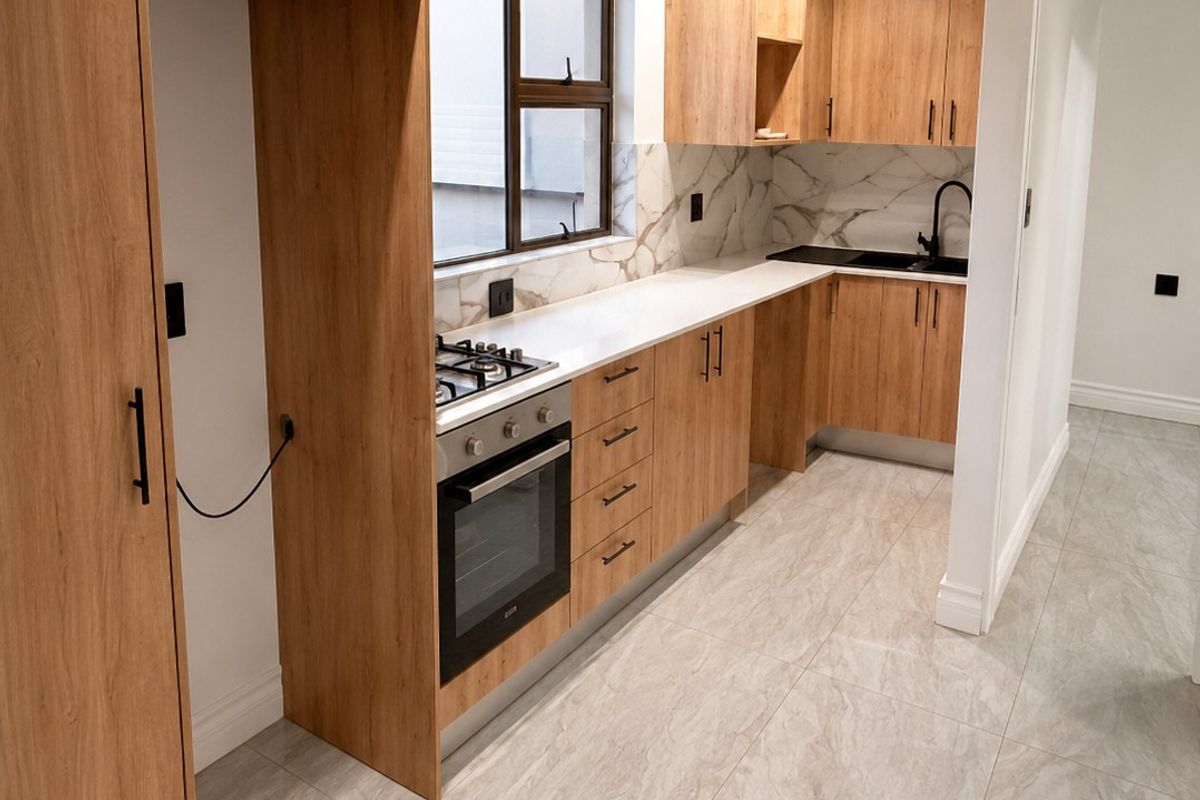 Modern kitchen featuring light wood-grain cabinetry, stone countertops, marble-look splashbacks, and high-quality integrated appliances with sleek black hardware.
