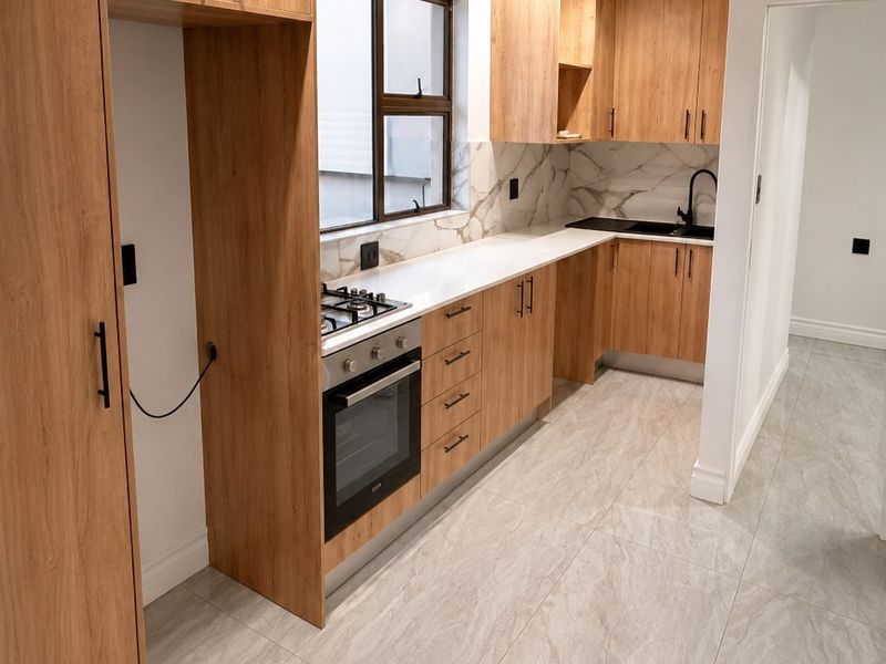 Modern kitchen featuring light wood-grain cabinetry, stone countertops, marble-look splashbacks, and high-quality integrated appliances with sleek black hardware.