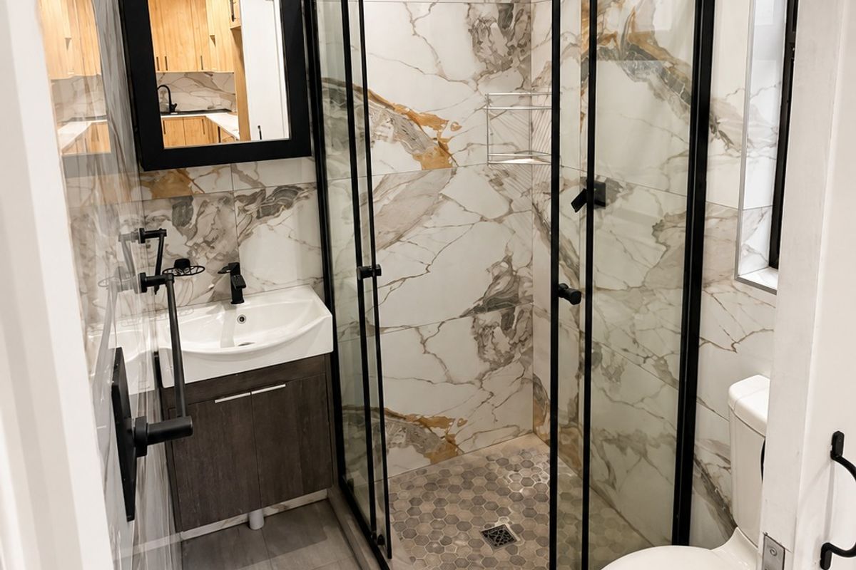 Modern bathroom featuring a walk-in shower with black frame, vanity with basin, and elegant marble-look wall tiling.