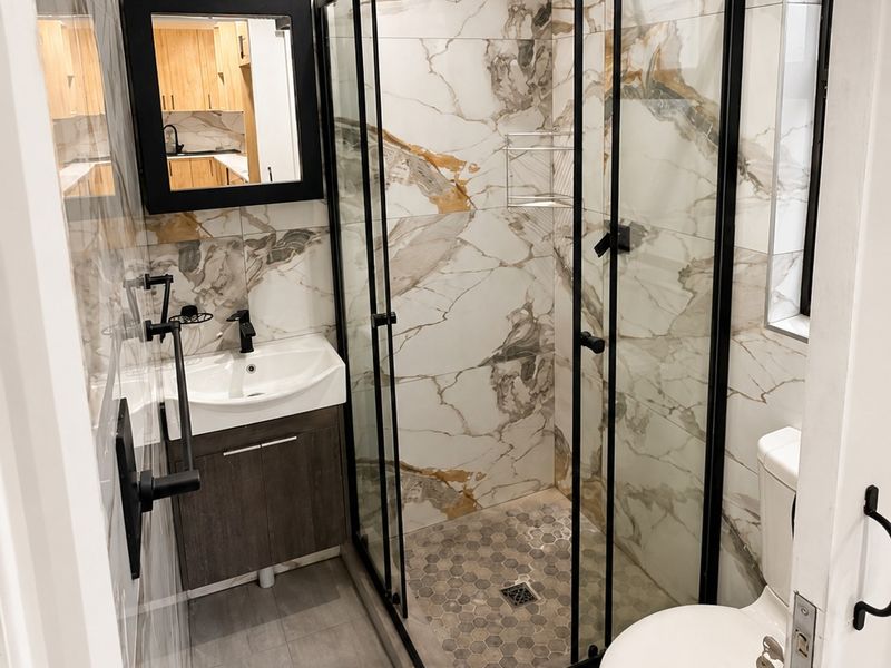 Modern bathroom featuring a walk-in shower with black frame, vanity with basin, and elegant marble-look wall tiling.