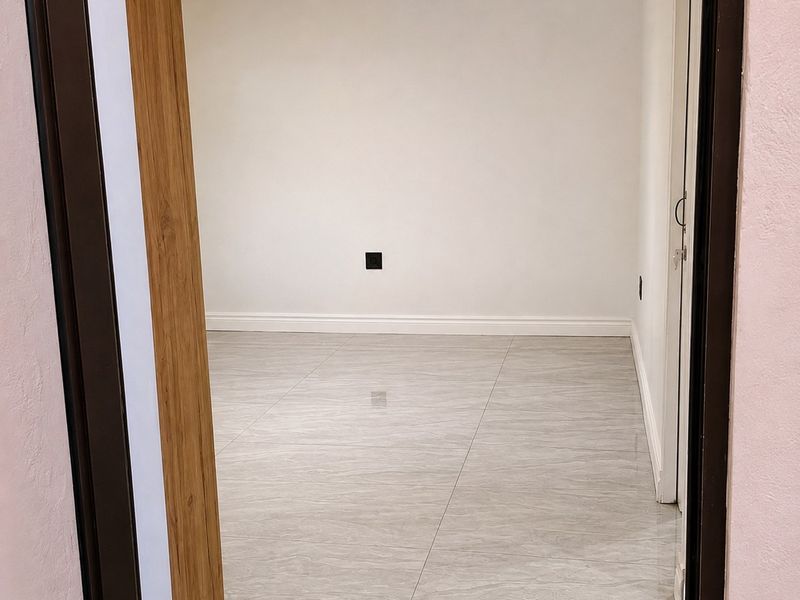 A bright, empty bedroom featuring modern grey porcelain tile flooring, crown molding, and adjustable track lighting.