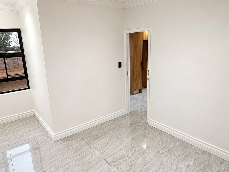 A bright, empty bedroom featuring modern large-format porcelain floor tiles, crisp white walls, crown molding, and a view into an adjacent room with built-in cabinetry.