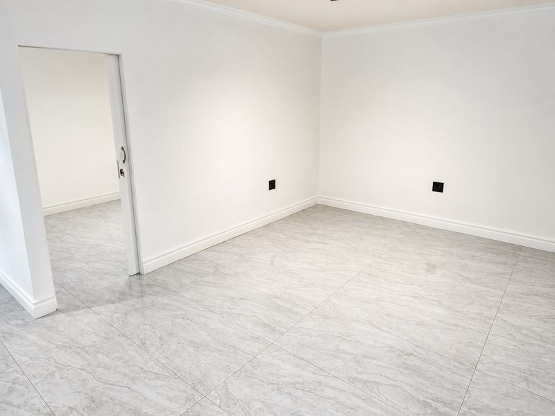A bright, empty living space featuring modern grey marble-look porcelain floor tiles, crisp white walls, and contemporary track lighting.