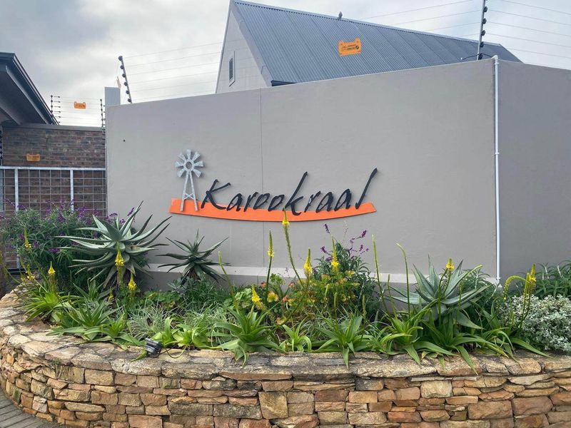 Front entrance area featuring a stone retaining wall, landscaped garden, and property signage with integrated electric fencing.