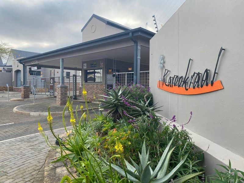 The entrance to Karookraal estate featuring a paved driveway, secure gated access, and well-maintained landscaping with a prominent property sign.