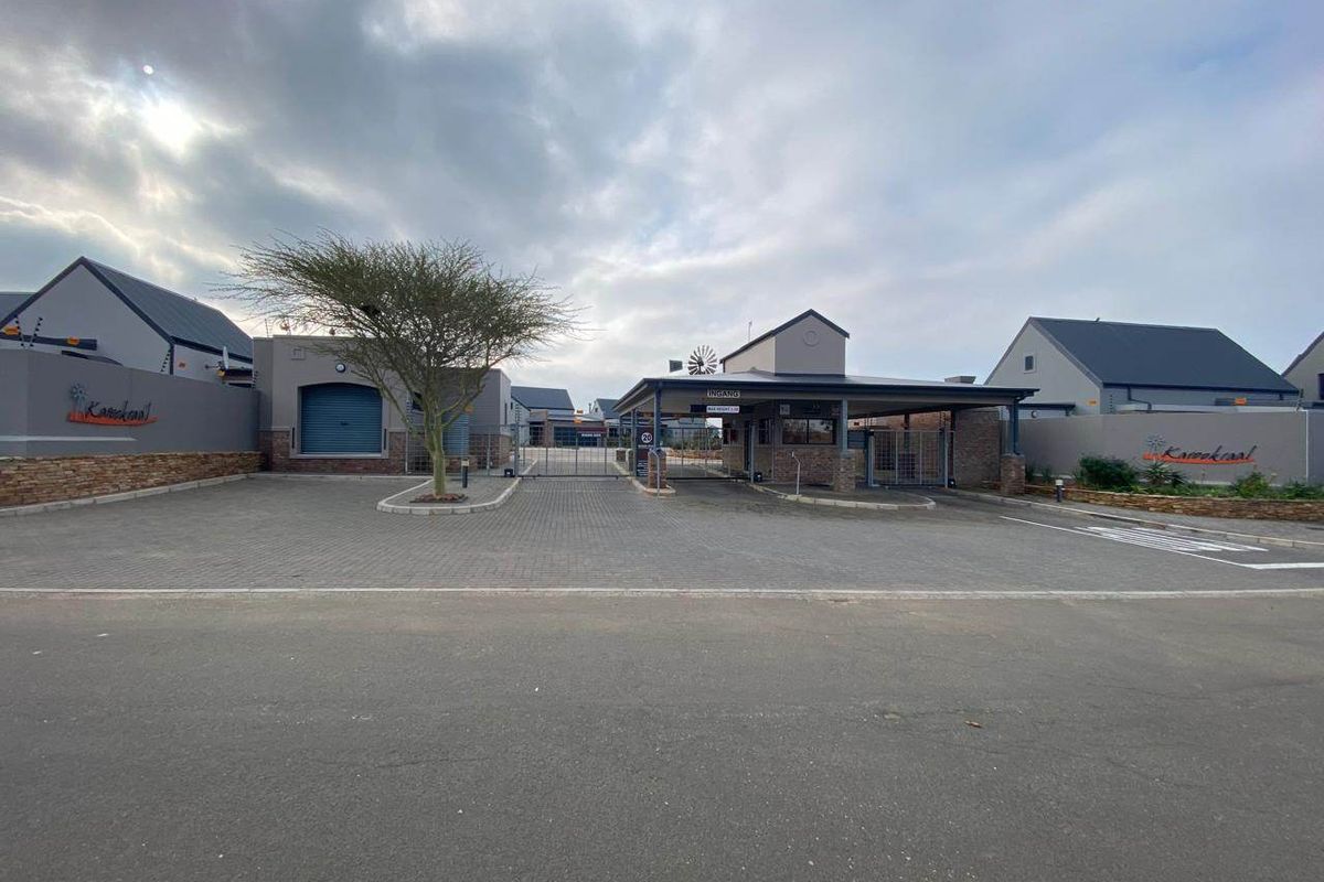 The secure entrance to the Karookraal estate, featuring a paved driveway, guard house, and perimeter walling with electric fencing.