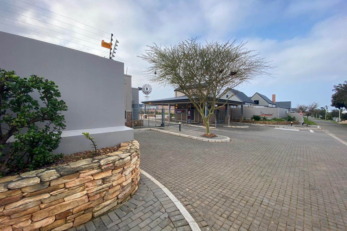 The entrance to the residential estate features paved driveway access, stone-clad boundary walls, and secure gated entry with electric fencing.