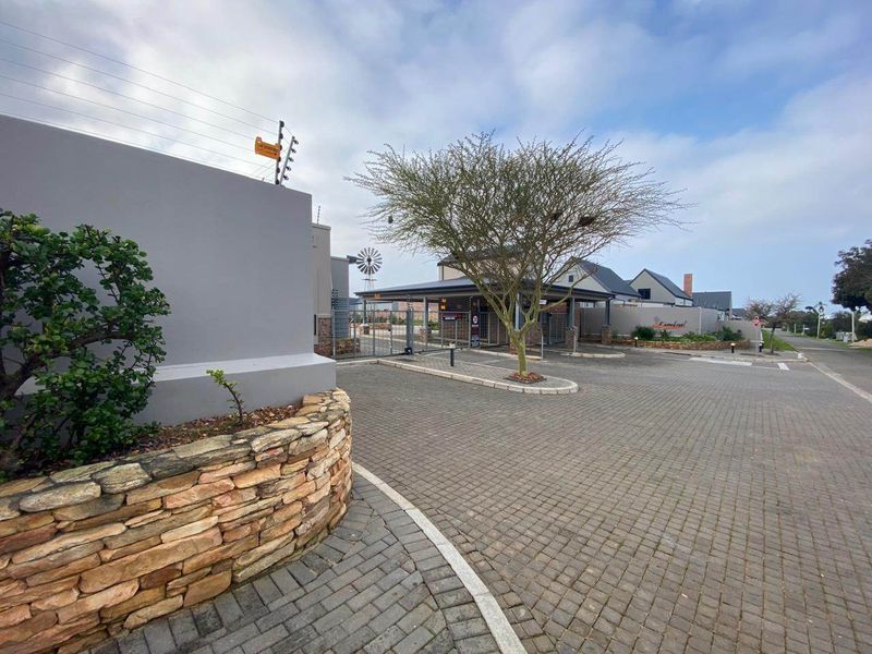 The entrance to the residential estate features paved driveway access, stone-clad boundary walls, and secure gated entry with electric fencing.