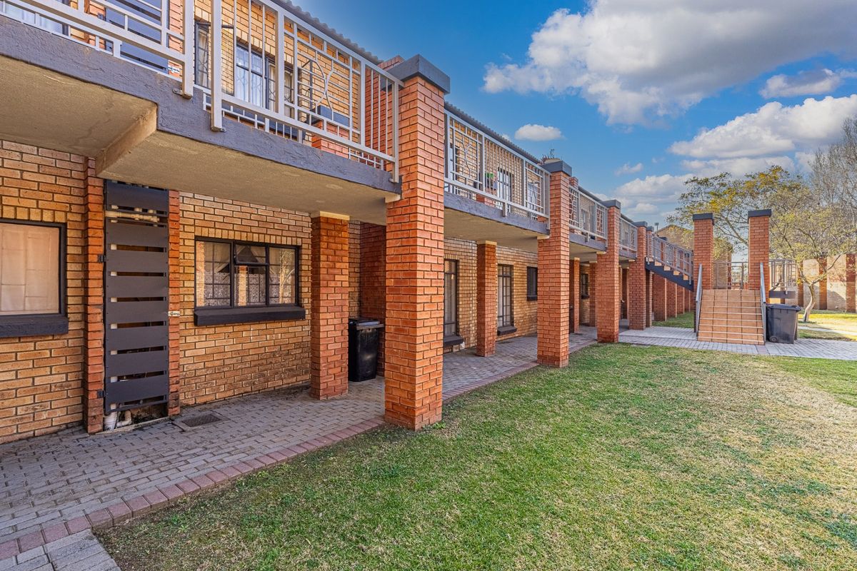 Rear view of a multi-story apartment complex featuring face brick construction, ground-level paved patios, and upper-level balconies with metal railings.