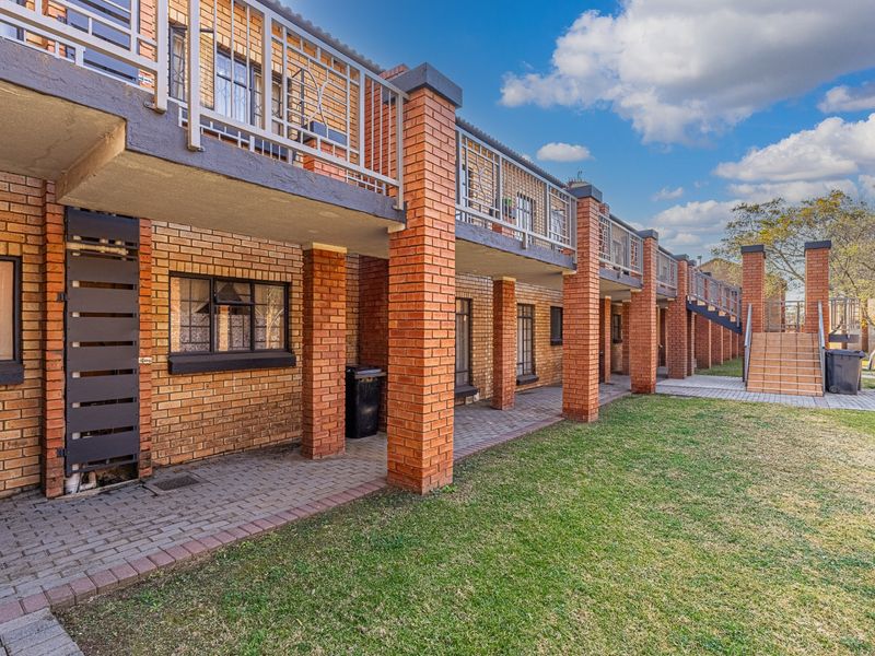 Rear view of a multi-story apartment complex featuring face brick construction, ground-level paved patios, and upper-level balconies with metal railings.