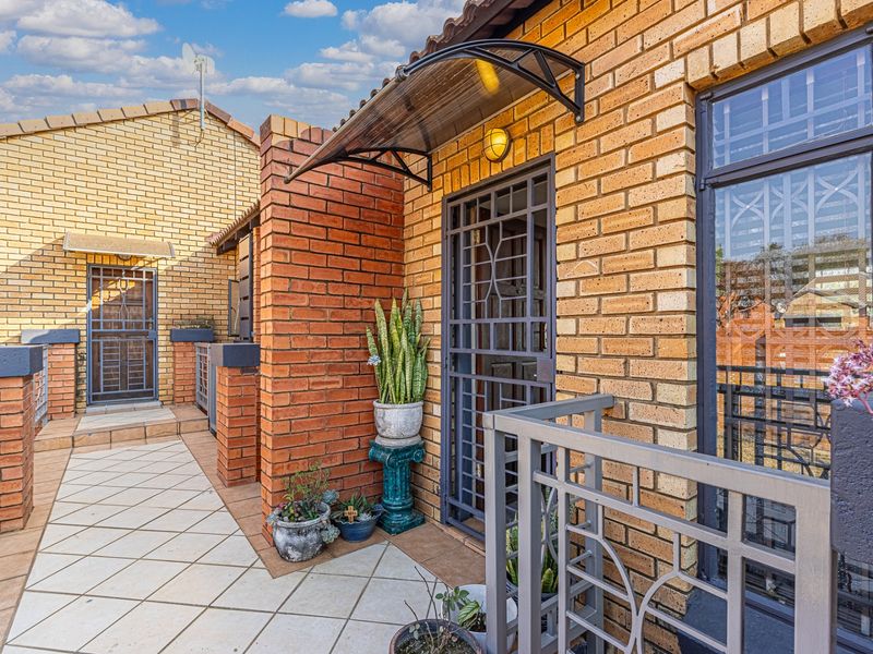 A well-maintained apartment balcony featuring brick exterior walls, tiled flooring, a protective awning, and secure metal gate access.