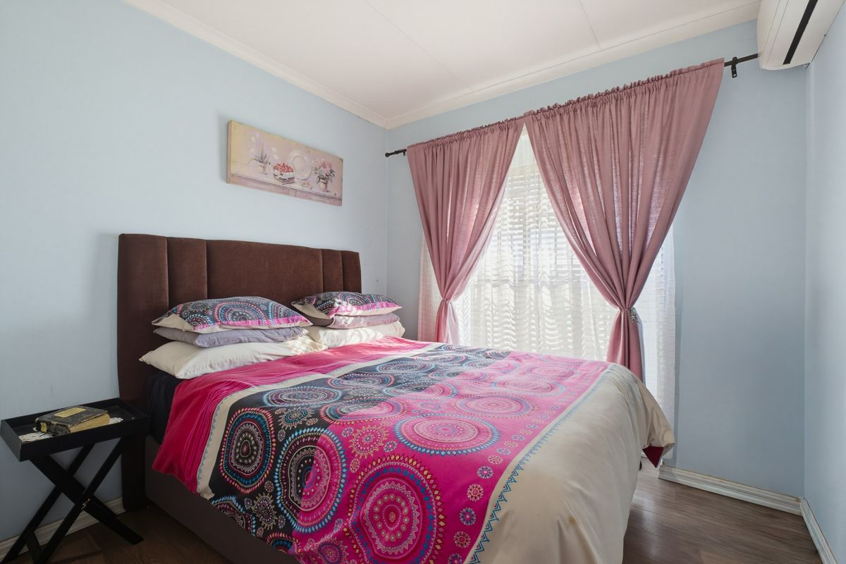 A cozy bedroom featuring laminate flooring and a wall-mounted air conditioning unit, providing a comfortable living space.