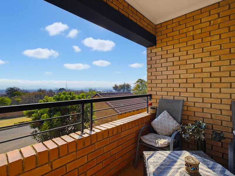 A covered balcony featuring exposed brick walls, a metal safety railing, and scenic elevated views of the surrounding landscape.