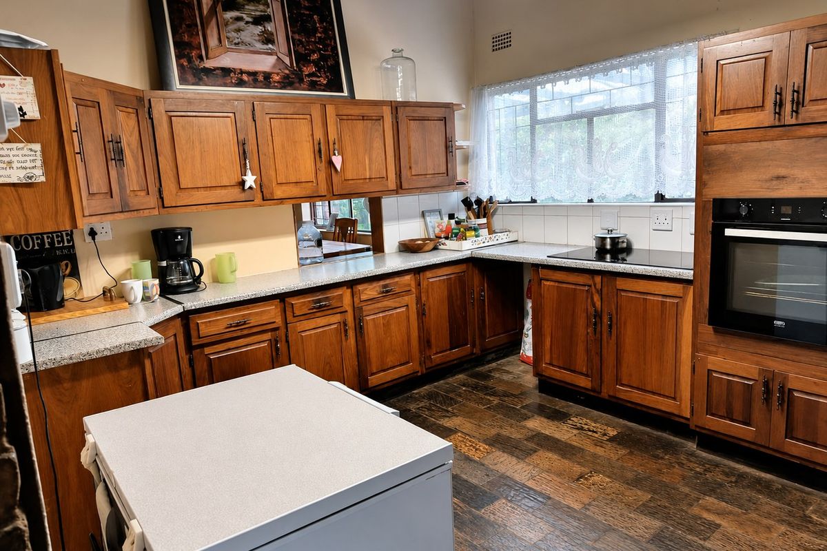 A functional kitchen featuring traditional wooden cabinetry, laminate countertops, a built-in oven, and an electric cooktop with tiled backsplash and timber flooring.