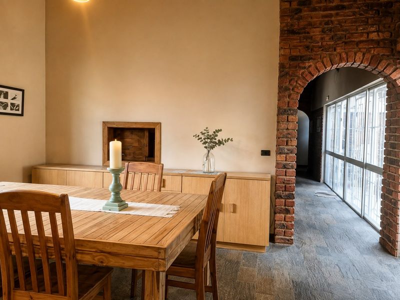 A dining area featuring stone tile flooring, built-in wooden cabinetry, and a distinctive exposed brick archway leading to a sunlit corridor.