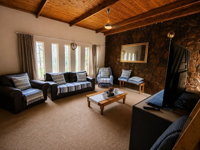 A cozy living room featuring a rustic stone accent wall, exposed timber beam ceiling, and large vertical windows that provide natural light.