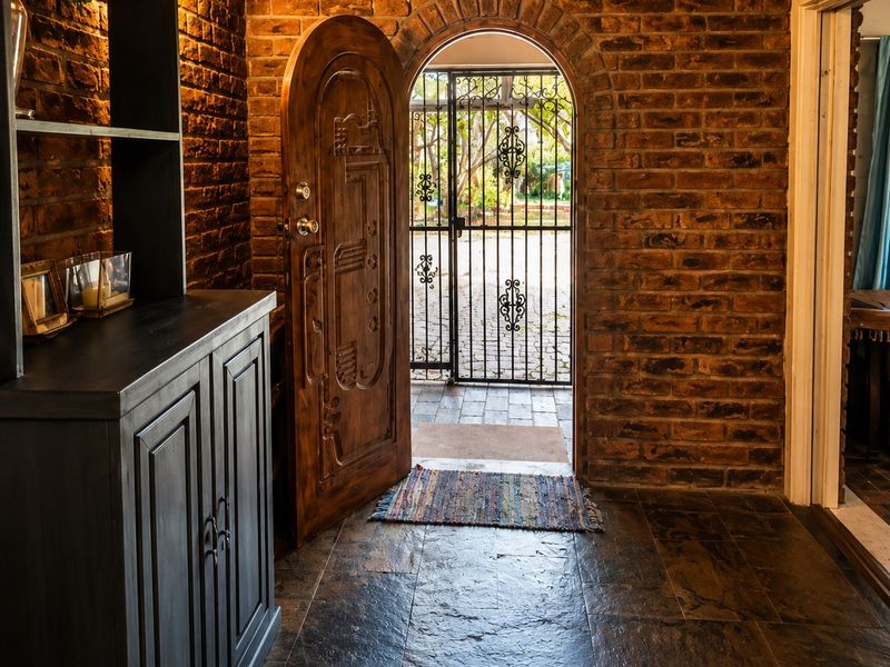 Inviting entryway featuring rustic exposed brick walls, arched timber door, and durable stone tile flooring, leading to an outdoor security gate.