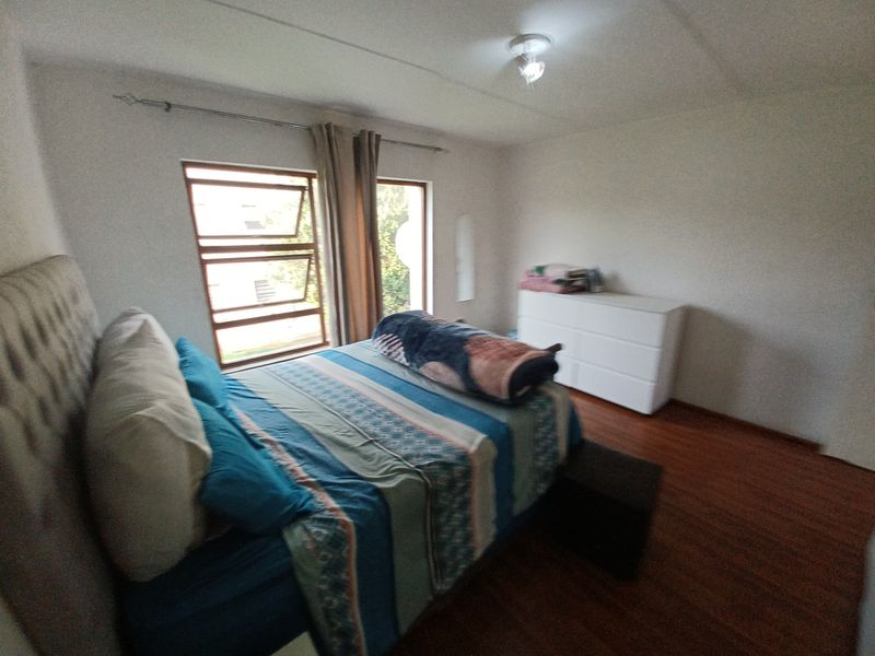 A bedroom featuring laminate flooring, natural light from casement windows, and a neutral wall finish.
