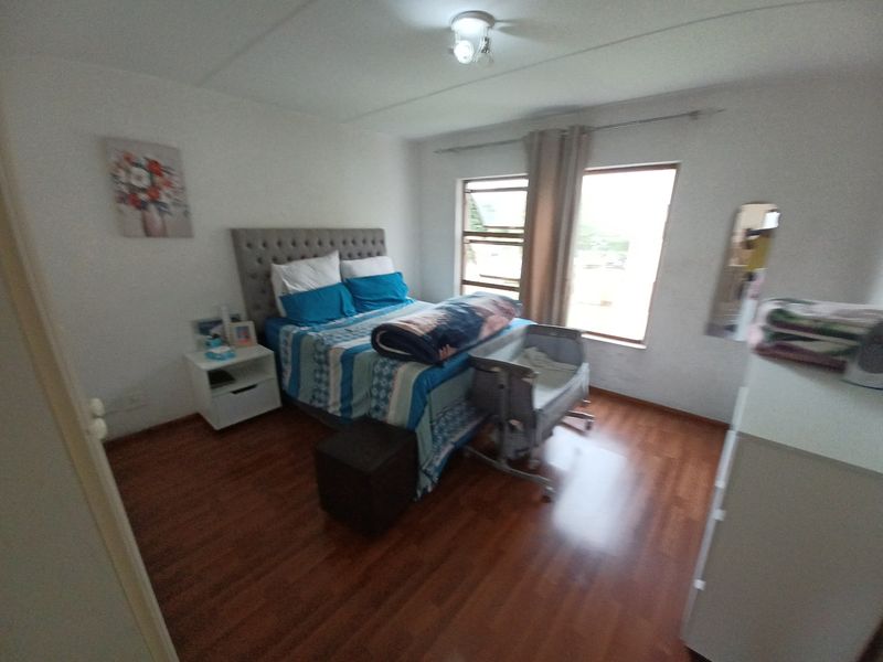 A bedroom featuring laminate flooring, natural light from casement windows, and a standard ceiling light fixture.