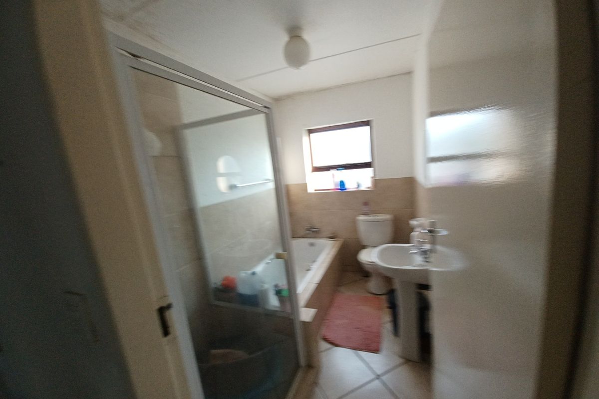 A functional bathroom featuring a shower enclosure, bathtub, pedestal basin, and toilet, currently showing signs of ceiling water damage and dated finishes.
