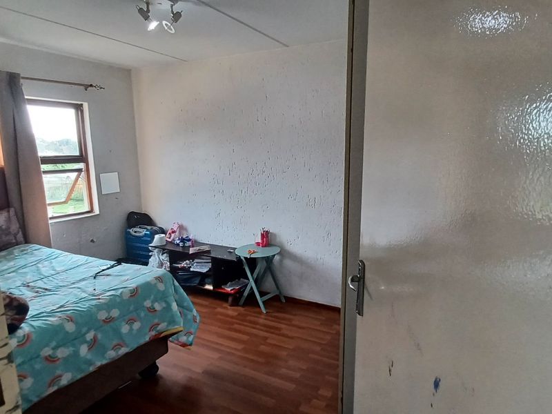 A bedroom featuring laminate flooring and a window, currently requiring cosmetic updates to the walls and door frame.