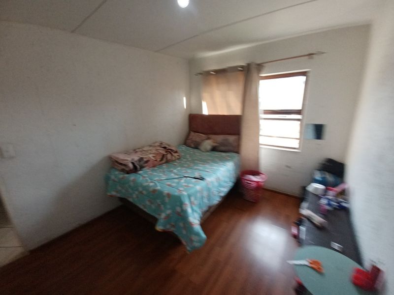 A compact bedroom featuring laminate flooring and a window with security bars, requiring cosmetic updates to improve the overall aesthetic.