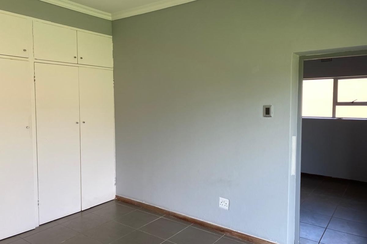 A clean, empty bedroom featuring neutral grey walls, tiled flooring, and ample built-in cupboard storage space.