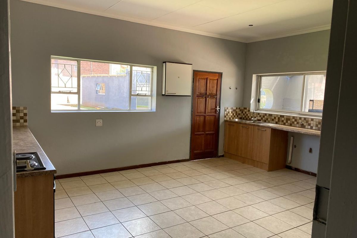 A spacious, empty kitchen featuring built-in cabinetry, laminate countertops, a built-in hob, and tiled flooring, offering a functional layout ready for updates.