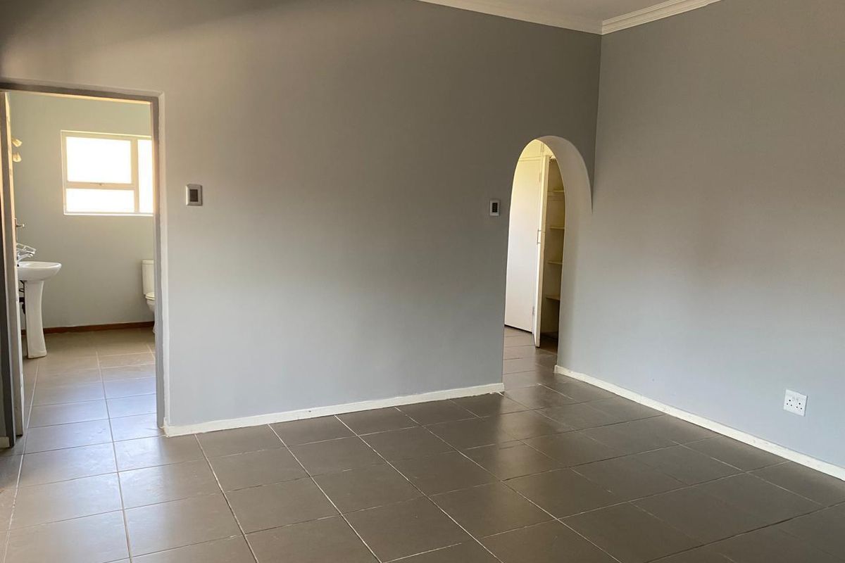 An empty living area featuring neutral grey walls, tiled flooring, and a distinctive arched doorway leading to adjacent rooms.