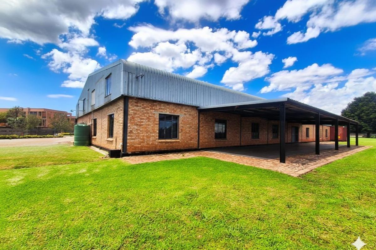 Rear view of a brick building featuring a large corrugated metal roof, a covered patio area, and an adjacent water storage tank.