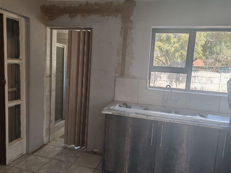 A kitchen area in need of finishing, featuring base cabinetry, a double sink, and tiled flooring, with unfinished wall surfaces requiring attention.